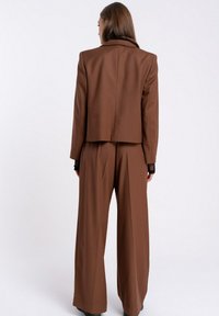 Brązowy garnitur o dopasowanym kroju z krótką marynarką i szerokimi spodniami. Gładka tkanina, subtelna tekstura i strukturalny design z wyraźnymi liniami.