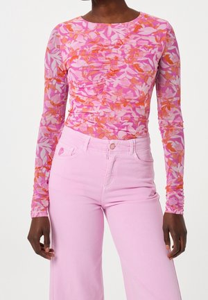 Woman wearing a long-sleeve fitted floral top in pink and orange with light pink high-waisted pants, standing against a plain background.
