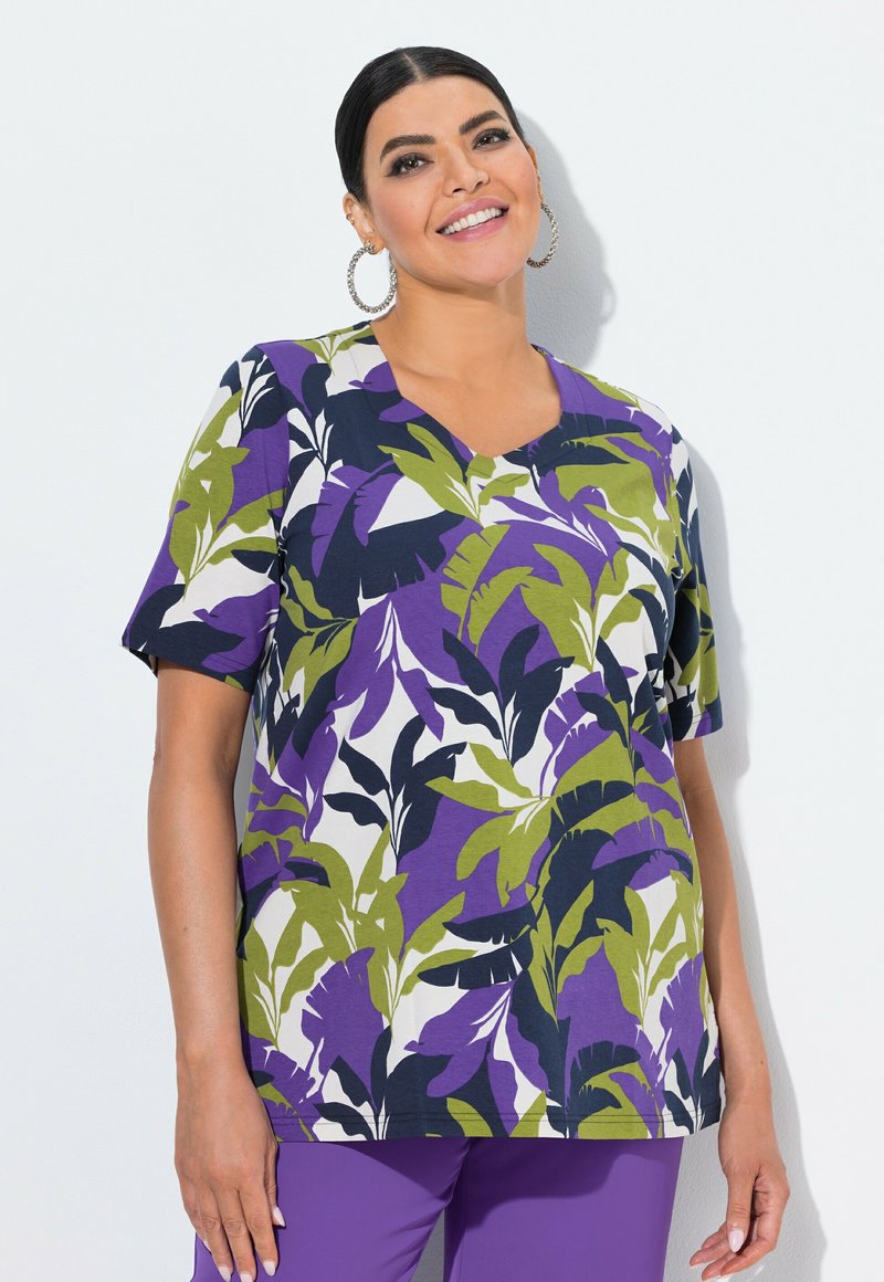 Camiseta de manga corta con un patrón floral que presenta tonos de verde, púrpura y azul marino sobre un fondo crema; diseño de escote en V con un corte relajado.