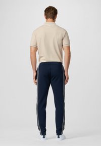Polo beige con dettagli a contrasto sul colletto, abbinato a pantaloni jogger blu navy con strisce laterali bianche e sneakers bianche.