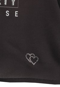 Camisa de tela negra con texto gráfico blanco y un motivo de corazón decorativo embellecido con cristales cerca del dobladillo. Textura suave en toda la prenda.