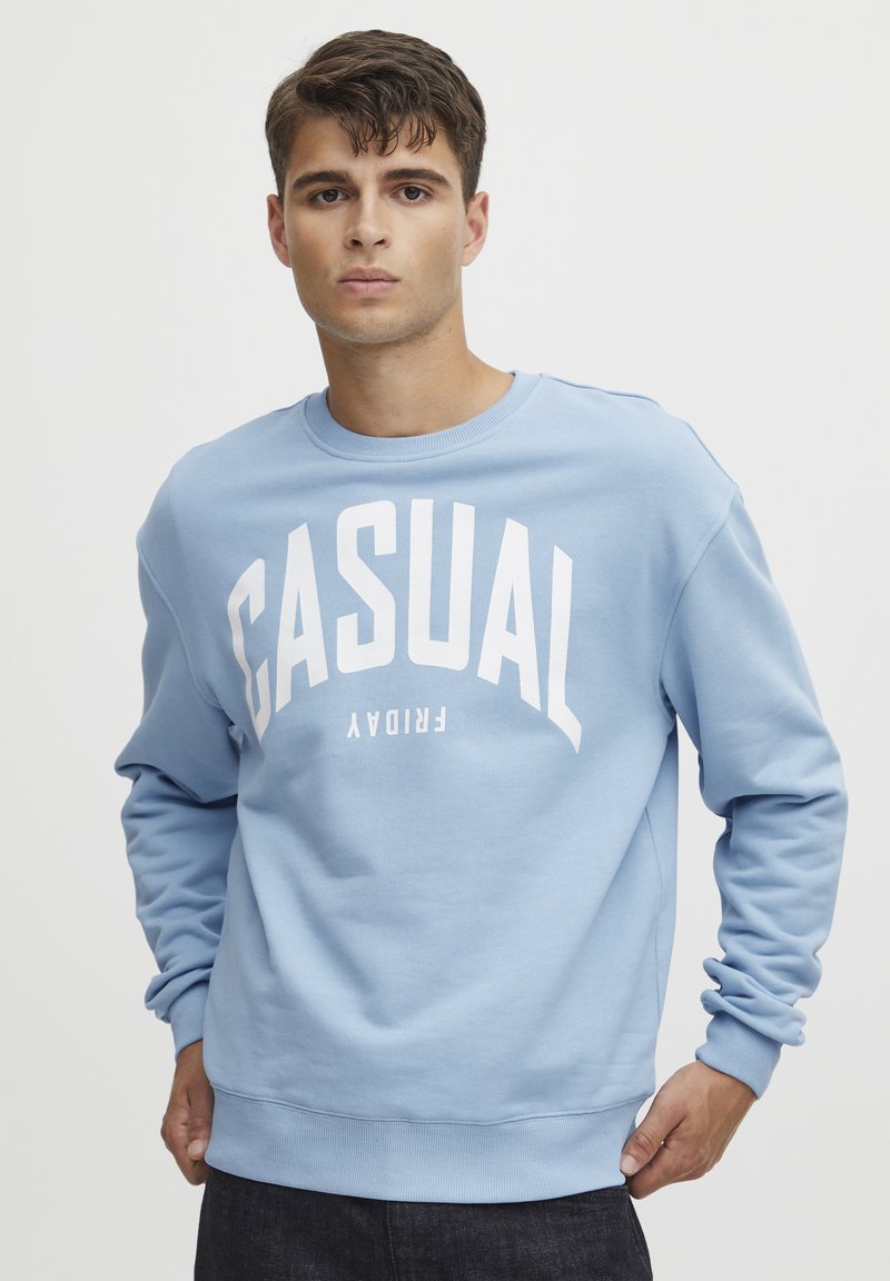 Svijetloplavi dukserica izrađena od mekanog materijala, s odvažnim bijelim tekstom "CASUAL FRIDAY", uz rebraste manžete i rub, te dizajn s okruglim izrezom.