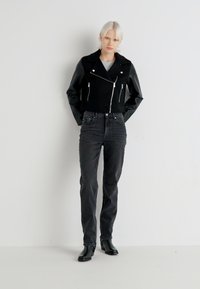 Svart kort jakke med lærermer, sølvglidelåser og krage med klipp. Kombinert med høy midje svarte jeans og ankelstøvler.
