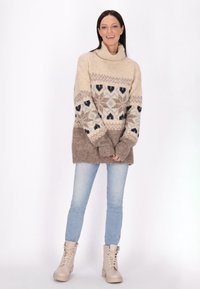 Pulover crem, cu model, cu guler înalt; are inimioare geometrice în nuanțe de maro și albastru. Asociat cu blugi ușor albaștri și cizme de gleznă bej.