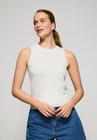 Top in maglia bianca senza maniche con un design aderente, colletto e orlo a costine, abbinato a jeans in denim blu a vita alta. Aspetto semplice e pulito.