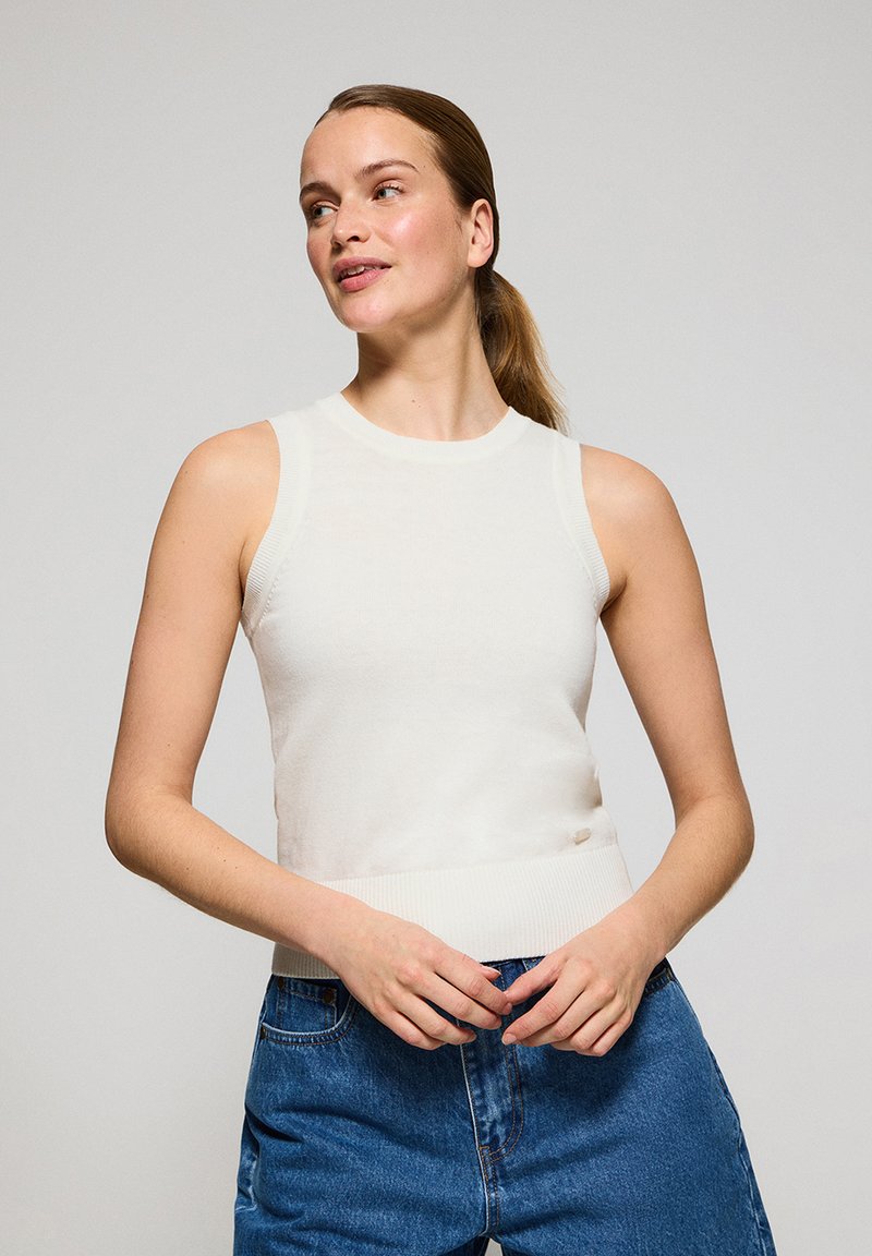Top in maglia bianca senza maniche con un design aderente, colletto e orlo a costine, abbinato a jeans in denim blu a vita alta. Aspetto semplice e pulito.