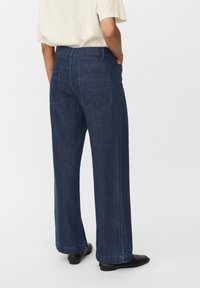 Jeans de mezclilla oscura de pierna ancha con una textura suave, que cuentan con dos bolsillos traseros y un diseño de cintura alta. Los puños están ligeramente deshilachados.