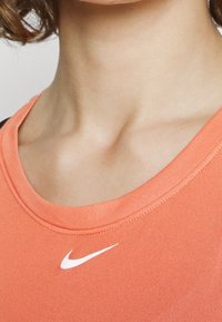 Maglietta atletica arancione realizzata in tessuto liscio, con scollo tondo e logo Nike bianco sul petto.