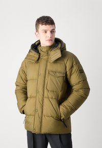 Oliwkowa kurtka puchowa z kapturkiem na zamek błyskawiczny, zatrzaskami, bocznymi kieszeniami i pikowanym wyglądem; posiada małą kieszonkę na piersi.