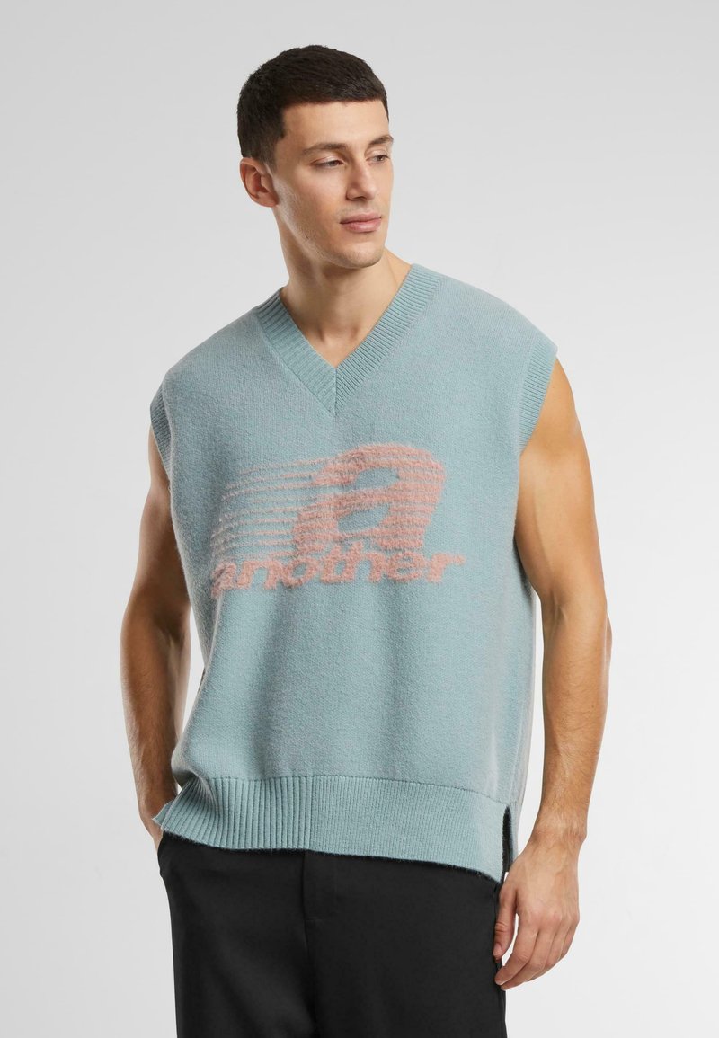 Lyseblå, ærmeløs strikket sweater med V-udskæring; har en blød tekstur og lyserødt grafisk tekst "another." Ribbet kant og sideslids.