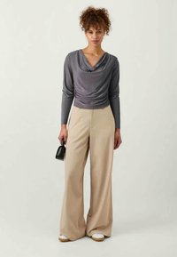 Gray cowl-neck long-sleeve top paired with beige wide-leg trousers, featuring a smooth texture and simple design. Model holds a small black bag.