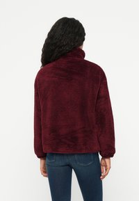 Bordeaux, ylellinen fleece-takki, jossa on korkea kaulus ja pitkät hihat, rento istuvuus ja joustavat hihansuut.