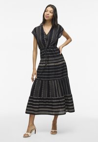 Abito maxi nero con accenti dorati a fantasia, scollatura a V, maniche a cappuccio e vita con fiocco. Gonna svasata con dettaglio di volant a strati.