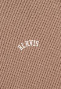 Tissu tricoté côtelé beige avec texte brodé blanc en relief "HLKVIS" centré en forme d'arche.