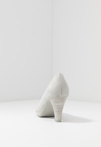 Ljust grå mocka högklackad sko med spetsig tå och texturerad randig klack. Slät yta, minimalistisk design och inga synliga mönster.