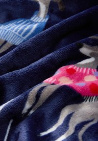 Tissu bleu marine doux avec des chiens imprimés portant des pulls colorés en bleu et rose, présenté en gros plan avec plis et texture visibles.