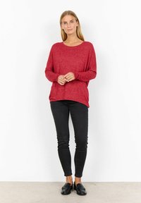 Röd långärmad topp med avslappnad passform, parat med svarta skinny jeans och svarta loafers. Tyget verkar strukturerat och avslappnat.