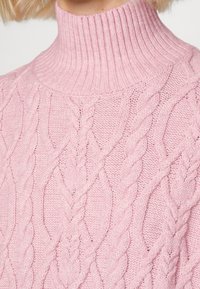 Light pink knitted turtleneck sweater featuring cable patterns and ribbed detailing at the collar, showcasing a soft texture.