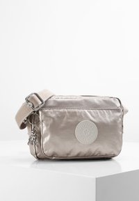 Metallic silver crossbody bag with a textured finish, featuring a logo patch, a silver charm, and a wide adjustable strap.