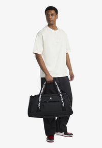 Μαύρη τσάντα duffel με διπλές λαβές, διαθέτει λογότυπο "jordan sport" και μπροστινή τσέπη με φερμουάρ· ανθεκτικό υλικό, ορθογώνιο σχήμα.