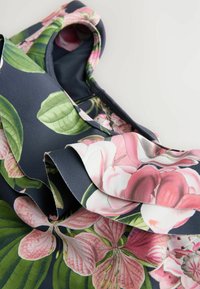 Marinfärgad tyg med rosa och gröna blommönster; har volangerade kanter. Texturen är slät och designen inkluderar stora lövmönster.