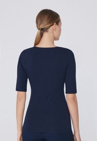 Námorně modrý krátký rukáv top s kulatým výstřihem, vyrobený z hladkého, elastického materiálu. Má přiléhavou siluetu a čisté švy.