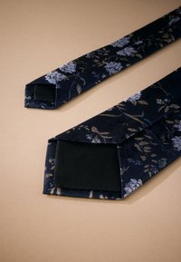 Cravate en tissu bleu marine avec motif floral doré et bleu clair ; texture lisse ; extrémités inclinées ; doublure intérieure noire.