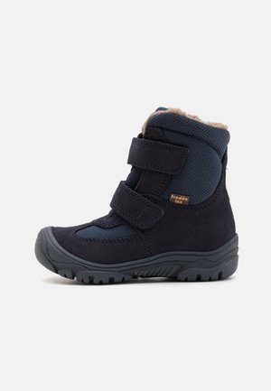 Botte d'hiver enfant bleu marine avec double sangles velcro, semelle texturée et doublure polaire beige douce visible en haut.