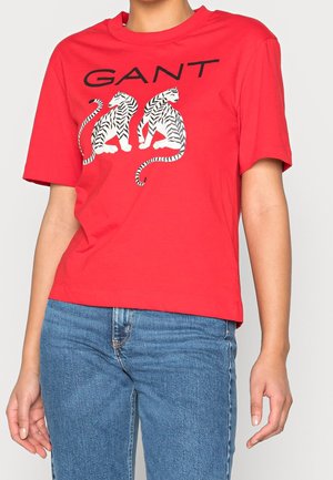 Camiseta de algodón roja con cuello redondo y mangas cortas, adornada con dos tigres a rayas en blanco y negro y la palabra "GANT."