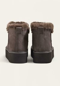 Braune Wildleder-Stiefeletten mit Kunstfellbesatz, flacher Plattformsohle und genähten Details. Rückansicht, die die Textur und Form zeigt.