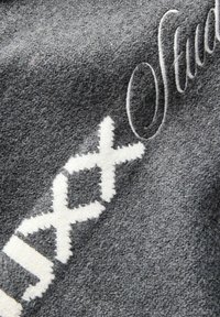Tissu texturé gris avec un motif blanc cousu et une broderie cursive partielle en haut à droite.
