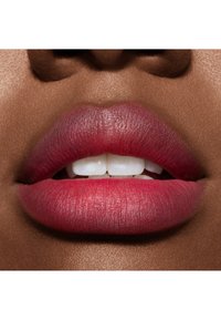 Gros plan sur des lèvres avec un dégradé de couleur rosée rouge. Texture lisse et forme définie avec une brillance subtile. Les dents blanches sont légèrement visibles.