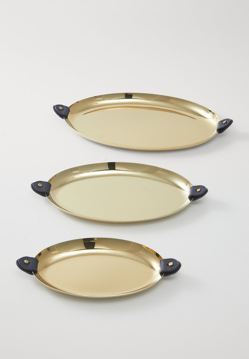 Σύνολο τριών οβάλ δίσκων σε χρυσή φινίρισμα με σκούρες μπλε δερμάτινες λαβές, που διαθέτουν λείες επιφάνειες και κομψό σχέδιο. Διάφορα μεγέθη στοιβαγμένα.