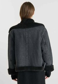 Giacca di jeans nera con colletto e polsini in pelliccia nera. Caratterizzata da un design squadrato e una vestibilità cropped, che mette in risalto un aspetto testurizzato e stratificato.