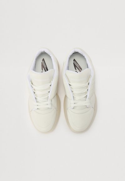 Baskets blanches avec une tige en cuir lisse et une semelle en caoutchouc, dotées de lacets, d'un col rembourré et d'un logo discret sur la languette.