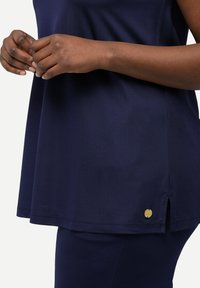 Top blu navy con vestibilità rilassata, caratterizzato da una leggera apertura laterale e un logo dorato all'orlo. Realizzato in un morbido tessuto testurizzato.