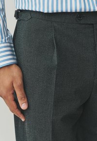 Sive hlače s teksturom imaju jedan prednji naboj i elegantnu siluetu, dopunju s pojasom u istoj boji i kopčanjem na gumb.