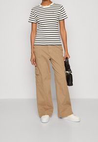 Pruhované černobílé tričko s kulatým výstřihem, spárované se béžovými cargo kalhotami se kapsami. Bílé tenisky a černá kabelka dotvářejí celý vzhled.