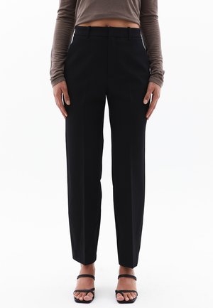 Pantalones negros ajustados con corte recto, que presentan un frente plano, pasadores para cinturón y una textura de tela suave. Diseño minimalista.