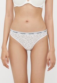 Bele čipkaste hlačke z oblogo v slogu Calvin Klein. Tkanina ima nežen vzorec in nizko pasovno obliko za udobje.