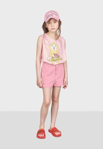 Rosa ärmlös topp med en lejongrafik och texten "The Animal Observatory", i kombination med rosa shorts och röda flip-flops med svart text.