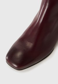 Bottine en cuir bordeaux avec un bout carré, texture lisse et design épuré. Présente peu de matériel et un talon solide et robuste.