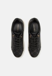 Paire de baskets basses noires avec design à lacets, motif de logo subtil, œillets dorés et semelles blanches, vues de dessus.