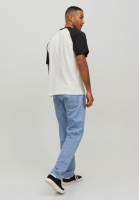 T-shirt z krótkim rękawem w czarno-białym kolorze, o luźnym kroju. Noszony z jasnoniebieskimi dżinsami i czarnymi trampkami.