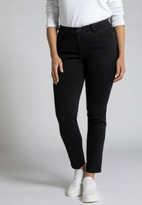 Black jeans with a slim fit, mid-rise waist, five-pocket design, and subtle stitching details, paired with white sneakers.