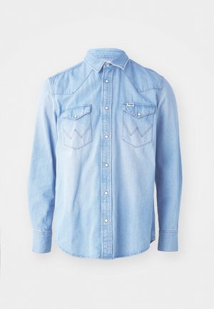 Light blue denim shirt featuring long sleeves, pointed collar, two chest pockets with zigzag stitch patterns, and button closure.