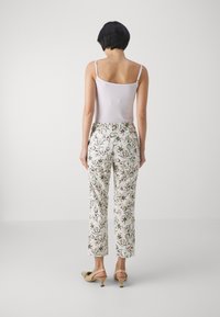 Mønstrede hvite bukser med blomsterdesign i grønt og svart, kombinert med en tettsittende hvit cami-top og beige sandaler med små hæler.