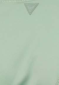 O tecido de banho verde-claro possui uma textura suave com um logo triangular GUESS® Beach e detalhes de costura subtis.