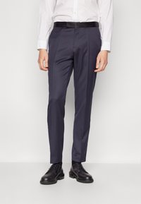 Pantaloni de costum navy dintr-un material fin, cu un croi drept, buzunare laterale și o tăietură măsurată, asortați cu pantofi negri și o cămașă albă.