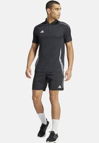 Zwart poloshirt met grijze accenten en schouderstrepen, gecombineerd met zwarte shorts. Beschikt over een standaardkraag en een textuurstof.
